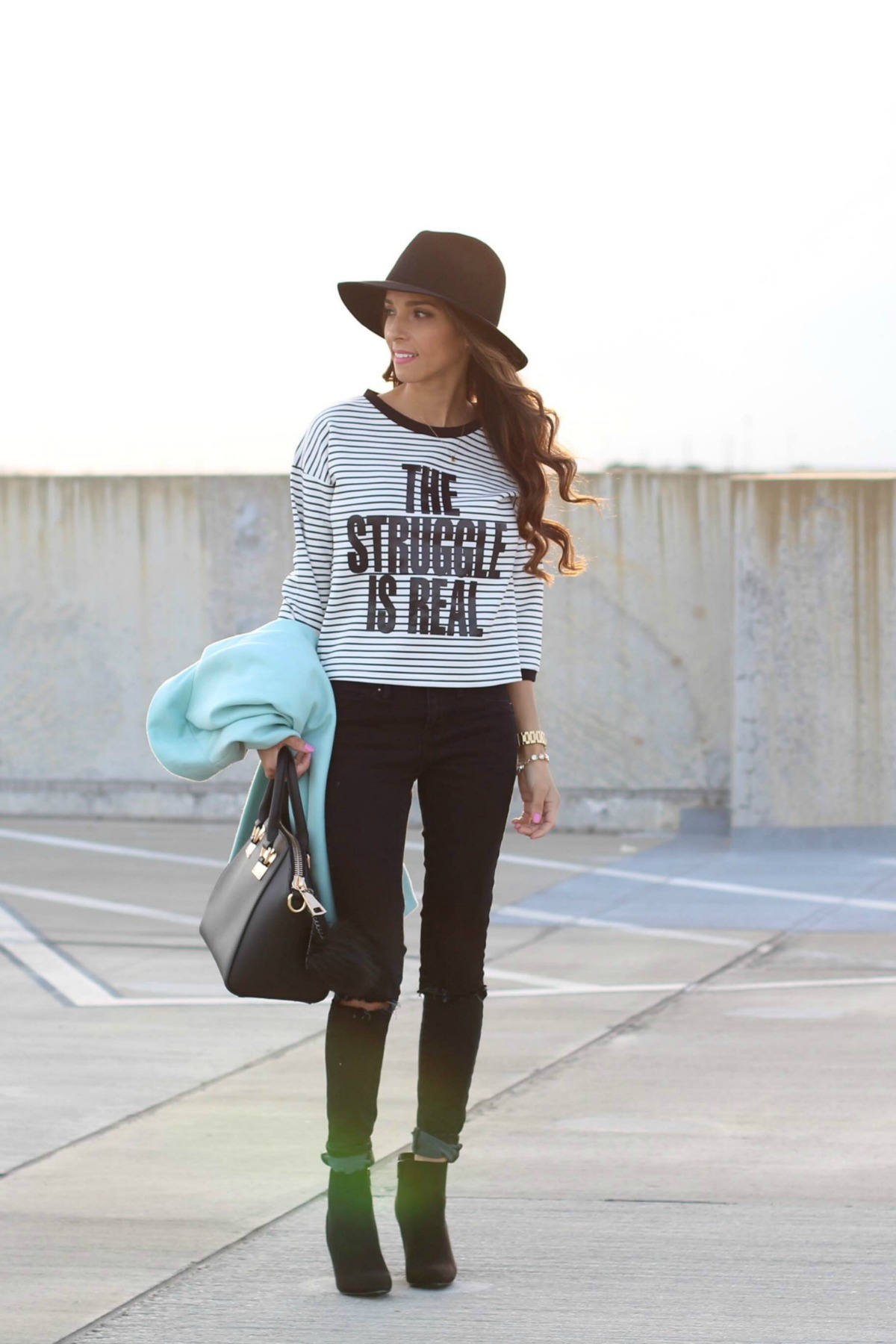 The Struggle is Real graphic tee with aqua coat, black jeans, booties and fedora