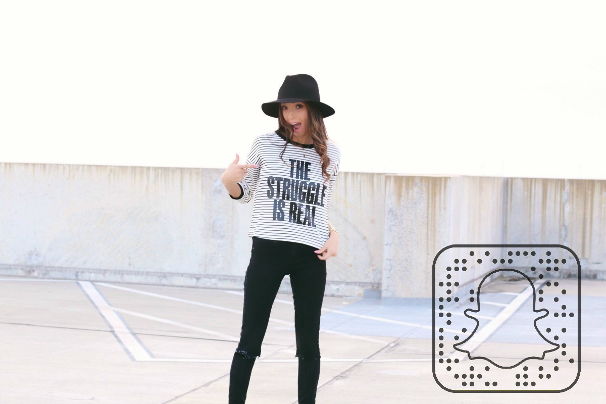 The Struggle is Real graphic tee with aqua coat, black jeans, booties and fedora